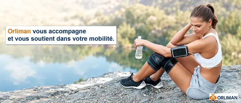Sportive assise au bord d’un lac, portant une genouillère Orliman. Texte : « Orliman vous accompagne et vous soutient dans votre mobilité. » Logo Orliman.